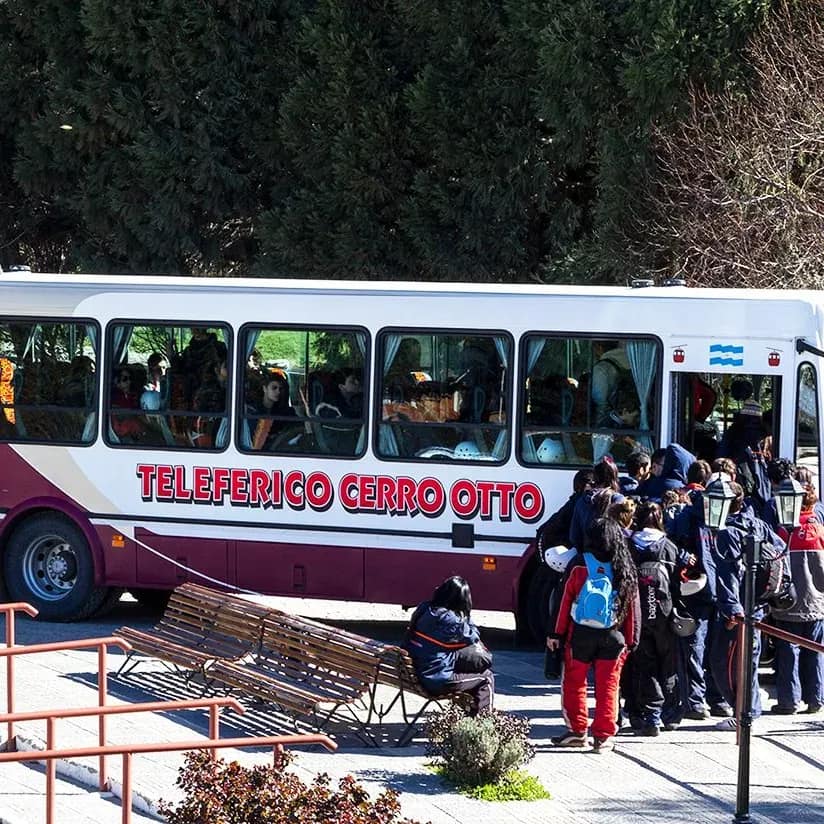 Bus turístico gratuito con logo del Teleférico Cerro Otto en el estacionamiento de la base con gente descendiendo.